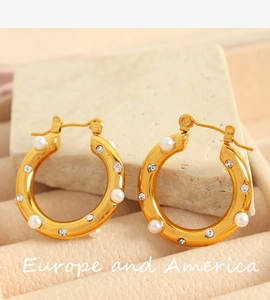 Close-up of gold C-shaped hoop earrings featuring inlaid white pearls and sparkling zircons