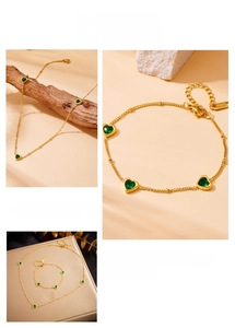 Detail of stainless steel gold jewelry set with green heart crystal on stone background