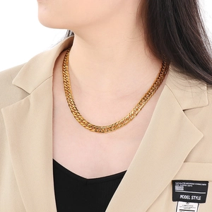 Detailed view of a thick gold-plated cuban chain necklace worn with a beige suit jacket