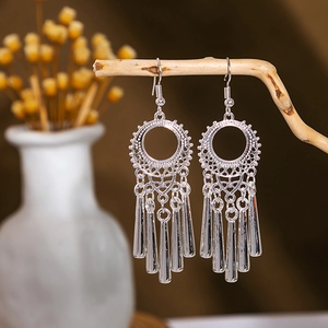 Detail of ethnic silver tassel earrings hanging on wooden branch with floral background