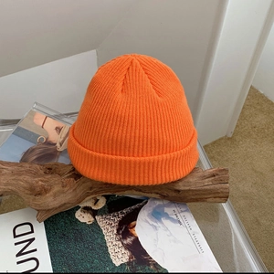 Detailed close-up of bright orange ribbed knit beanie resting on a rustic wood piece