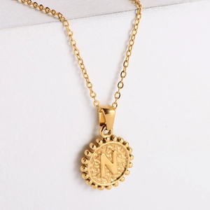 Macro view of 18k gold plated round necklace pendant with letter N and beaded edge