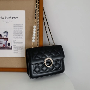 Detail of black quilted crossbody bag with gold chain and white pearl shoulder strap