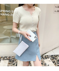 Close-up of white crocodile pattern leather wristlet bag held by a model in outdoor setting