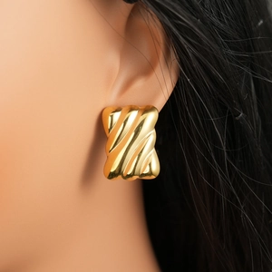 Close-up of golden geometric earrings with wavy texture worn by a model