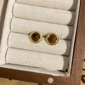 Macro view of gold round earrings with brown velvet spherical pendants on beige fabric