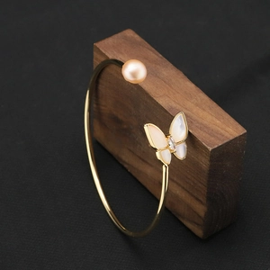 Elegant gold open bangle with pink pearl and butterfly design on dark wood block