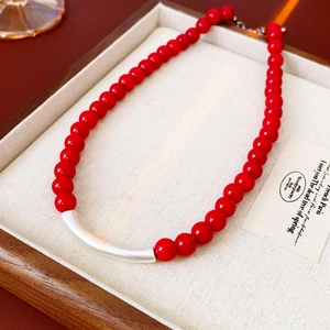 Collier ethnique en perles rouges avec tube argenté sur un plateau en bois