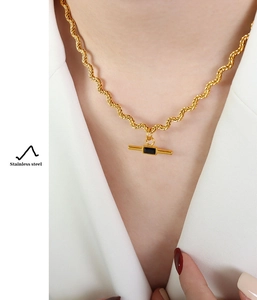 Detail of a gold stainless steel rope chain necklace with a black rectangular T-bar pendant