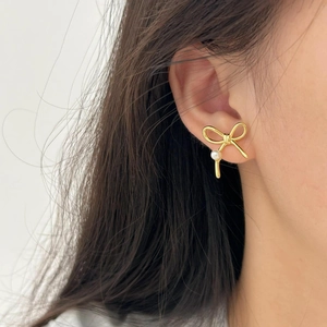 Elegant gold bow earrings with white pearl detail shown on model with white background