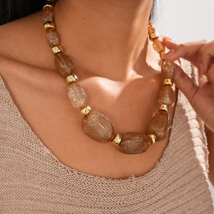 Detail of chunky amber acrylic beaded necklace with golden metal connectors on a model