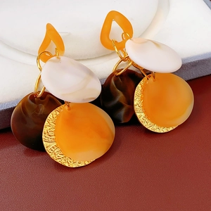 Detail of tassel earrings featuring mixed orange, brown resin and textured gold metal