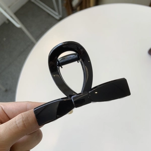 Detailed macro shot of the glossy black bow-shaped hair claw clip with reflective finish