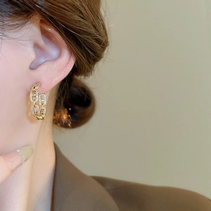 Macro detail of gold plated interlocking chain C-shaped earrings with pave zircon accents