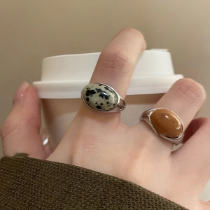 Close-up of minimalist silver rings with oval marble and caramel stone on finger