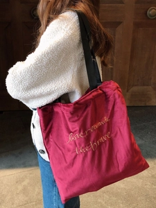 Burgundy velvet tote bag with gold embroidery and black strap on a model shoulder