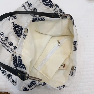 Detail of embroidered linen tote with magnetic closure, inner zipper pocket and leather strap