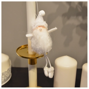 Detail of plush white Santa Claus ornament hanging on a gold candle holder in cozy lighting