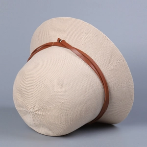 Detail of beige knitted bucket hat featuring brown leather strap and metal rivet accents