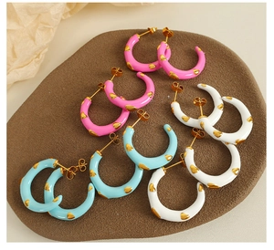 Detail of colorful C-shaped enamel earrings with golden heart patterns in pink, blue and white