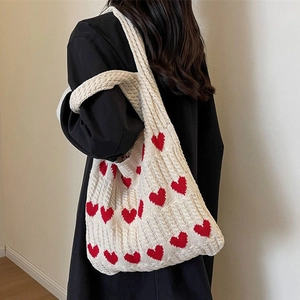 Detail of red heart jacquard patterns on a creamy white chunky knit shoulder tote bag