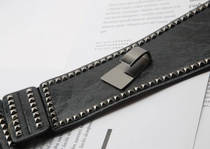 Detail of wide black punk waist belt with silver square studs and metal buckle closure