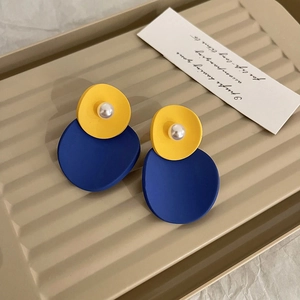 Close-up of geometric yellow and blue matte earrings with white pearls in a beige dish