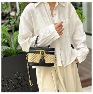 Detail of woven straw bucket bag featuring black faux leather trim and gold chain strap