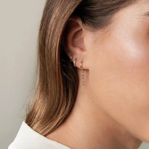Nahaufnahme von goldenen Creolen mit Regenbogen-Zirkonia am Ohr des Models