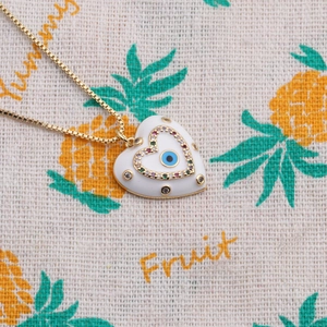 Macro shot of gold box chain and white heart pendant with blue evil eye and gems
