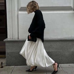 Close-up of white flowing midi A-line skirt paired with black heels and pearl anklet detail