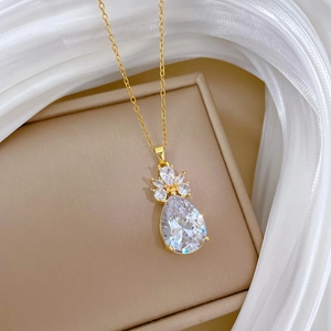 Détail macro du pendentif goutte en zircon doré sur soie blanche et écrin beige