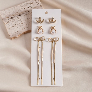Three-pair gold earring set with rhinestones, pearls and bow tassel on display card