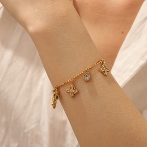 Detailed view of a gold clover charm bracelet with sparkling crystal droplets on a wrist