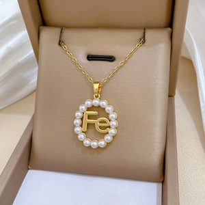Close-up of gold titanium necklace with a hollow 'Fe' pendant surrounded by pearls