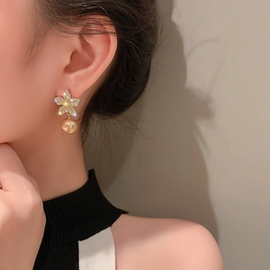 Vue détaillée de boucles d'oreilles fleur avec cristaux et perle dorée sur modèle