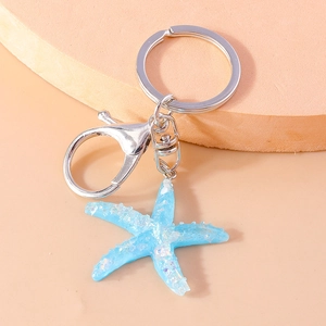Close-up of blue resin starfish keychain with silver metal ring on peach background