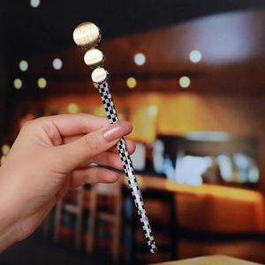 Detailed close-up of hair pin featuring black and white checkerboard and gold circles