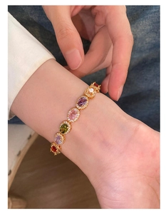 Close-up of gold bracelet with colorful oval-cut gemstones and zircon inlay on wrist