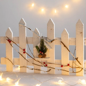 White wooden Christmas fence decoration with red berries and pine cones for tree base