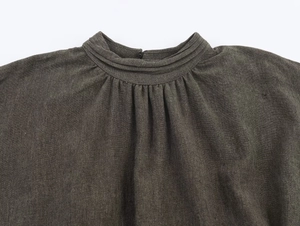 Detailed close-up of pleated neckline and button closure on dark linen mini dress