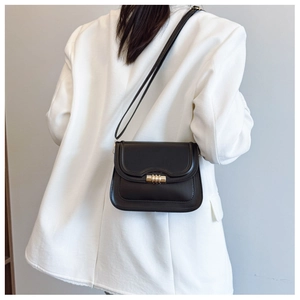 Détail d'un sac bandoulière en cuir noir avec boucle dorée sur un blazer blanc chic