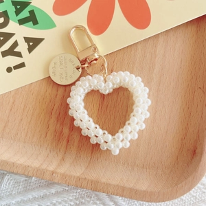 Macro detail of hand-woven pearl heart keychain with engraved golden metal tag