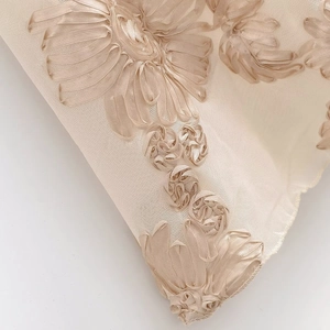 Détail de la broderie florale en ruban 3D beige sur un tissu en maille délicate
