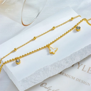 Double-layered gold chain anklet with butterfly pendant and crystal stones on white stone