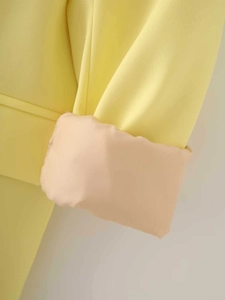 Detail of yellow satin blazer cuff with pink-orange lining and twill fabric texture