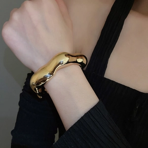 Close-up of a thick gold wave-textured cuff bracelet with a polished fluid design
