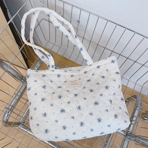 Gros plan du sac cabas matelassé blanc à motif floral bleu dans un panier en métal