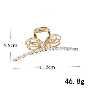 Detail view of a gold-finish metal bow hair claw with pearl inlay and 11.2cm length