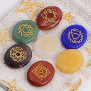 Polished seven chakra energy stones with gold symbols on a beige drawstring gift bag